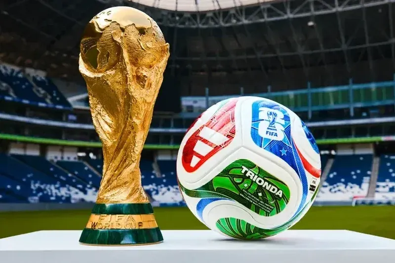 Taça da Copa do Mundo e bola oficial com estádio ao fundo